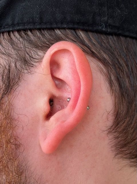A close up of a man 's ear with a piercing.