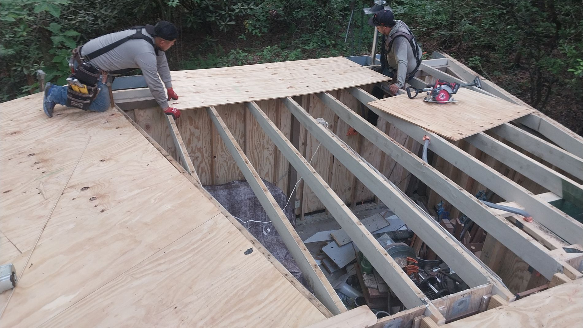 Two workers installing plywood sheeting on a wooden deck frame outdoors.