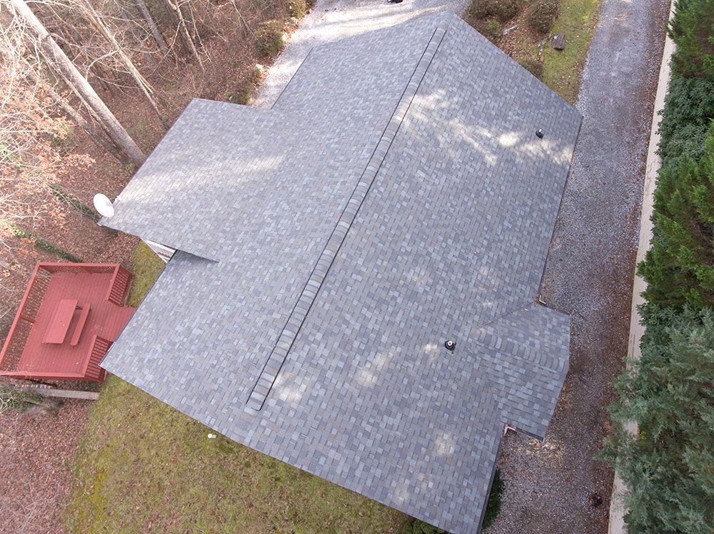 Aerial view of a gray asphalt shingle roof on a house, with a red deck and driveway visible.
