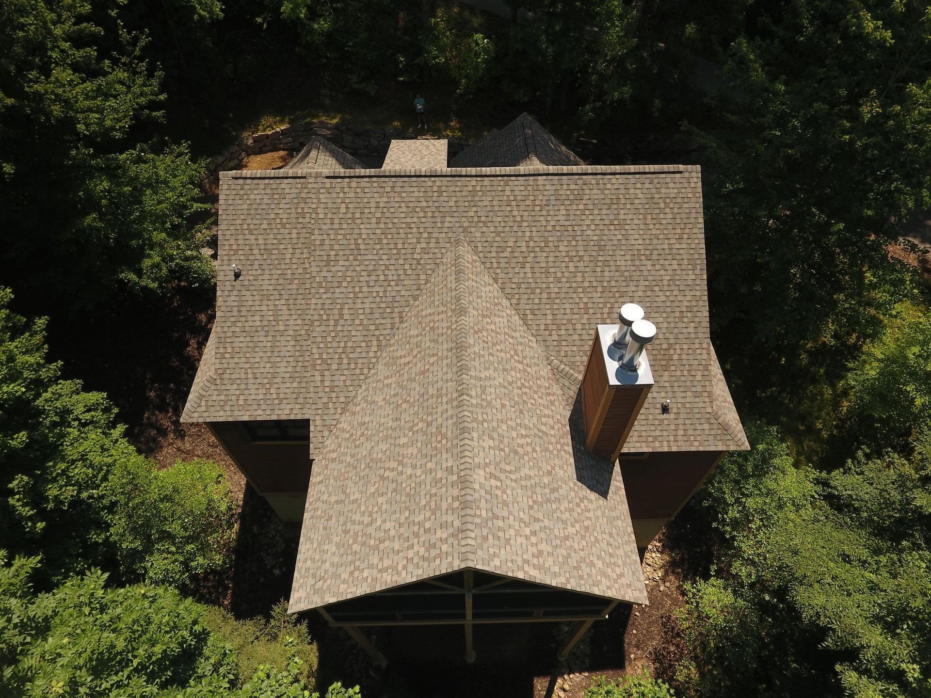 Aerial view of a brown-shingled roof house surrounded by green trees.