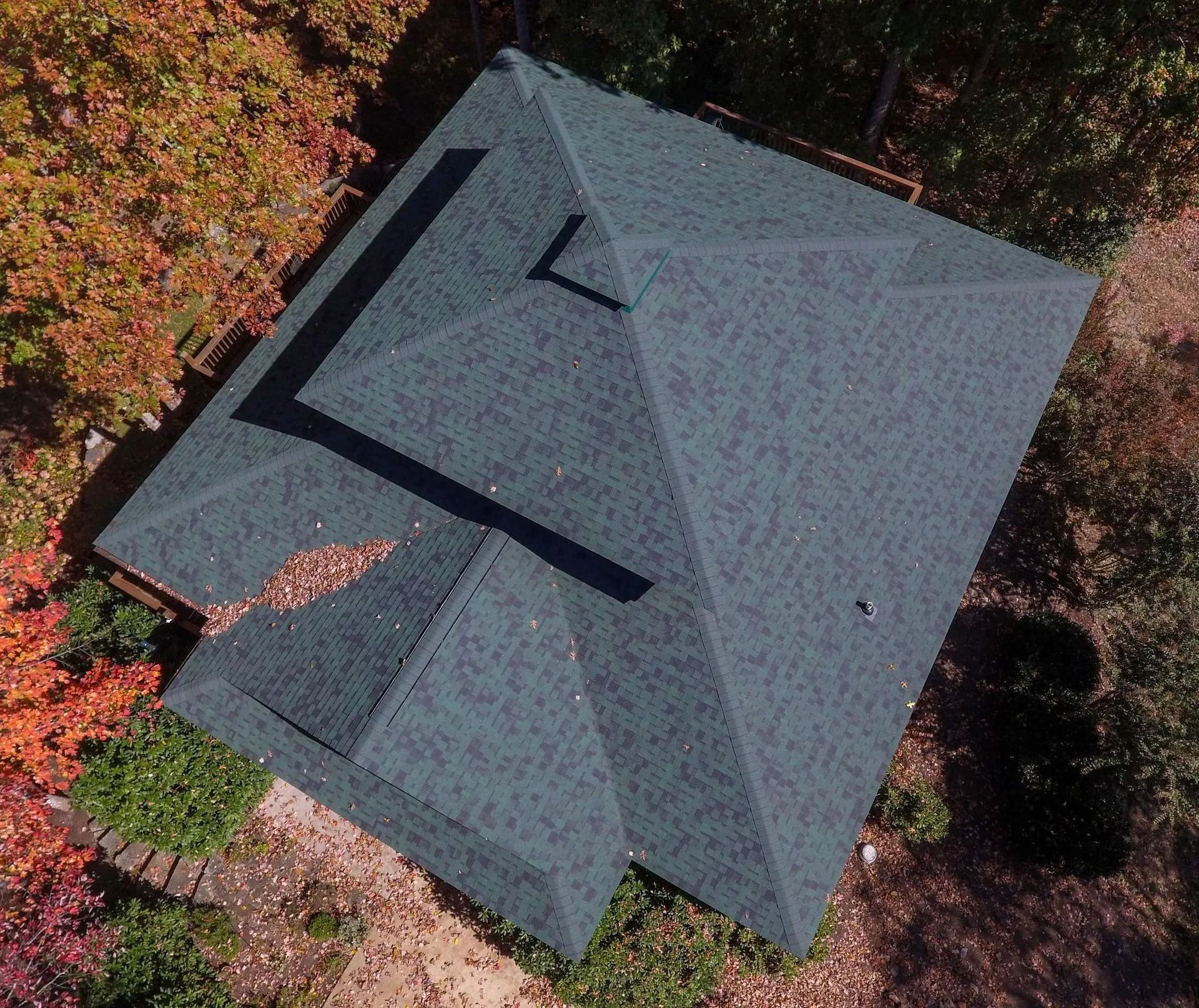 Overhead view of a dark green shingled roof surrounded by trees with fall foliage.