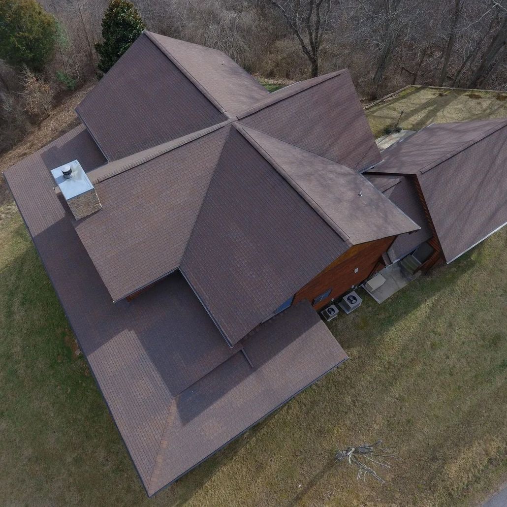 Overhead view of a house with a brown shingled roof, set on a grassy hill; chimney present.