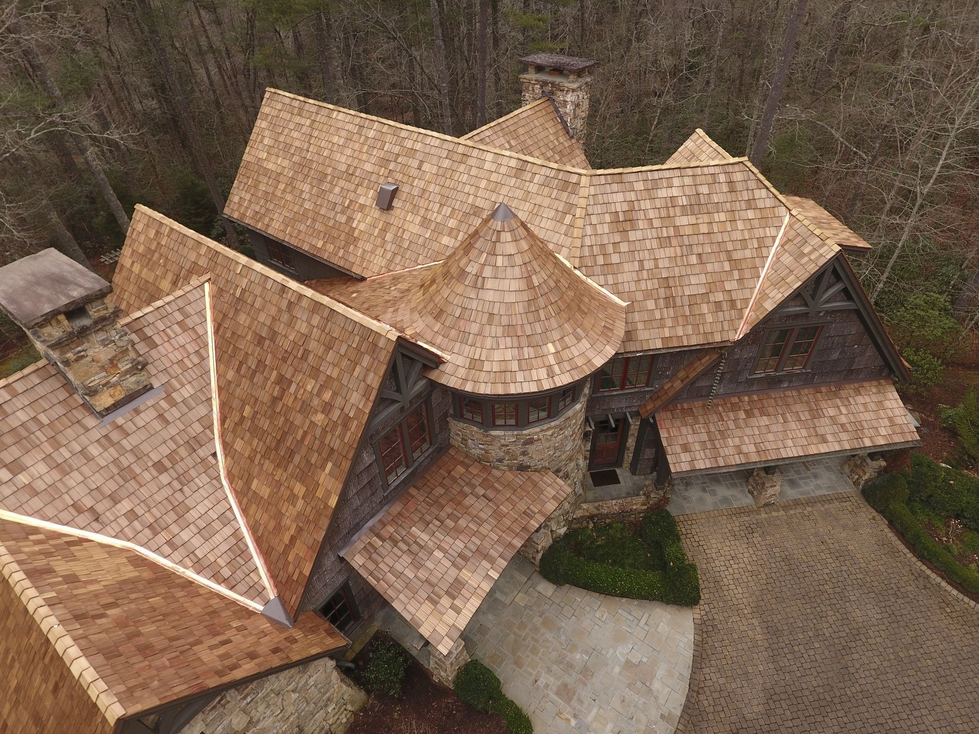 Aerial view of a unique house with multiple gabled and cone-shaped roofs; wood shingles and stone accents.