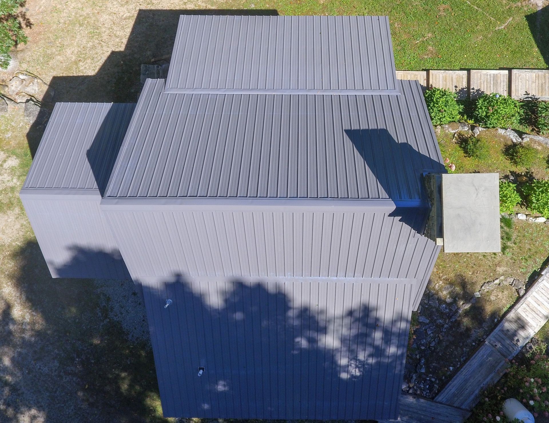 Overhead view of a house with a gray corrugated metal roof and a small concrete pad; set outdoors.