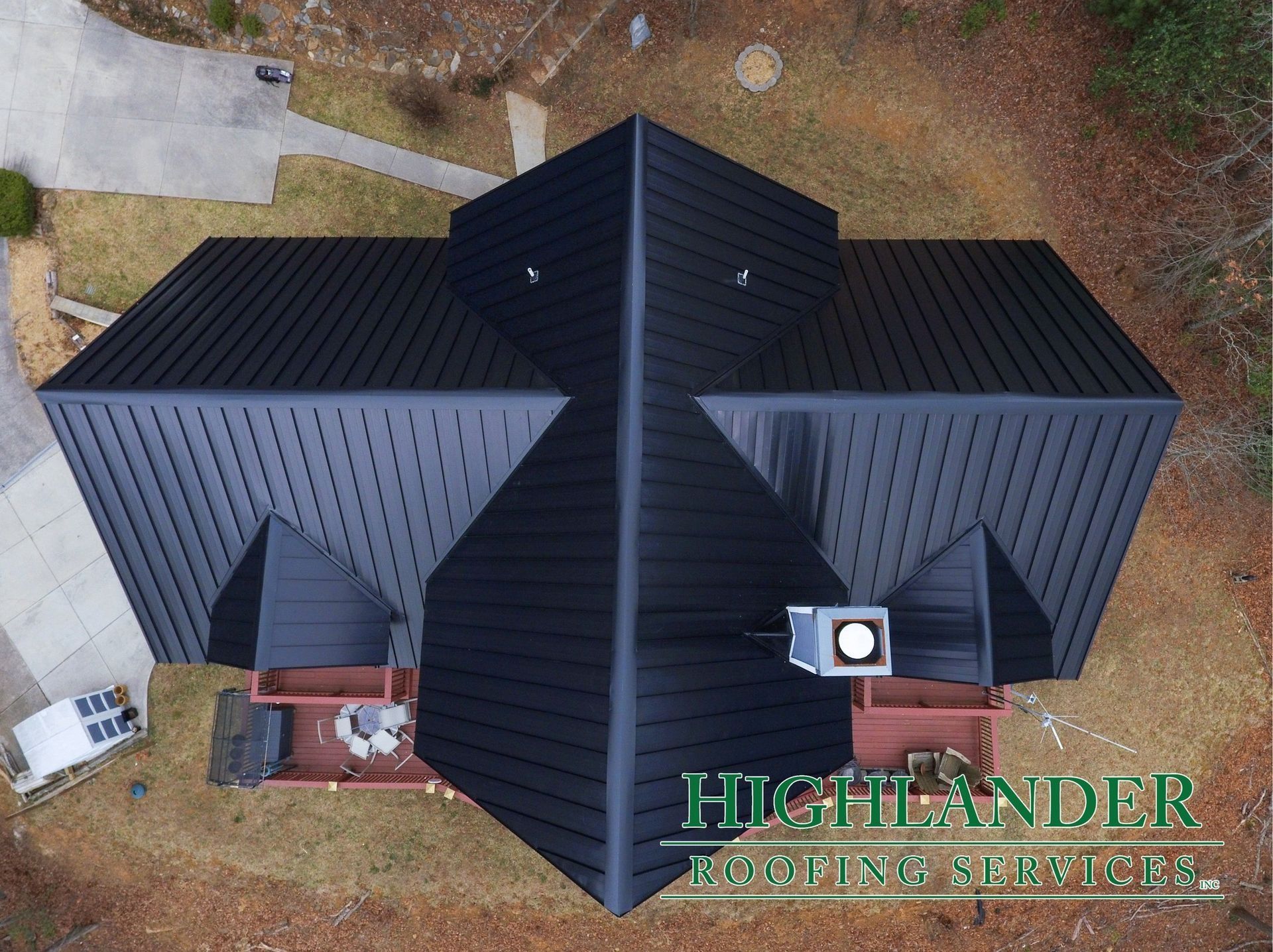 Aerial view of a black metal roof on a house with a concrete driveway and brown yard.