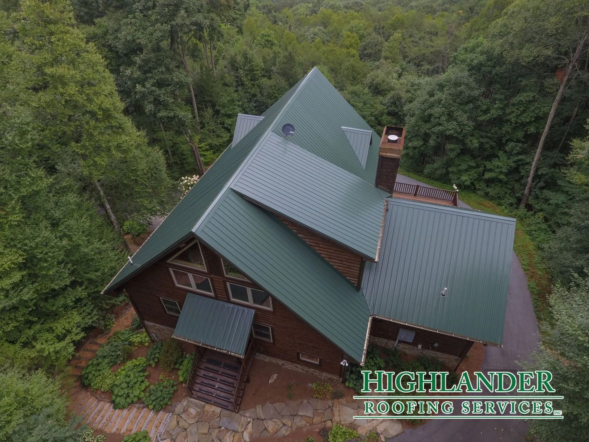 Aerial view of a green metal roof on a wooden house surrounded by trees.