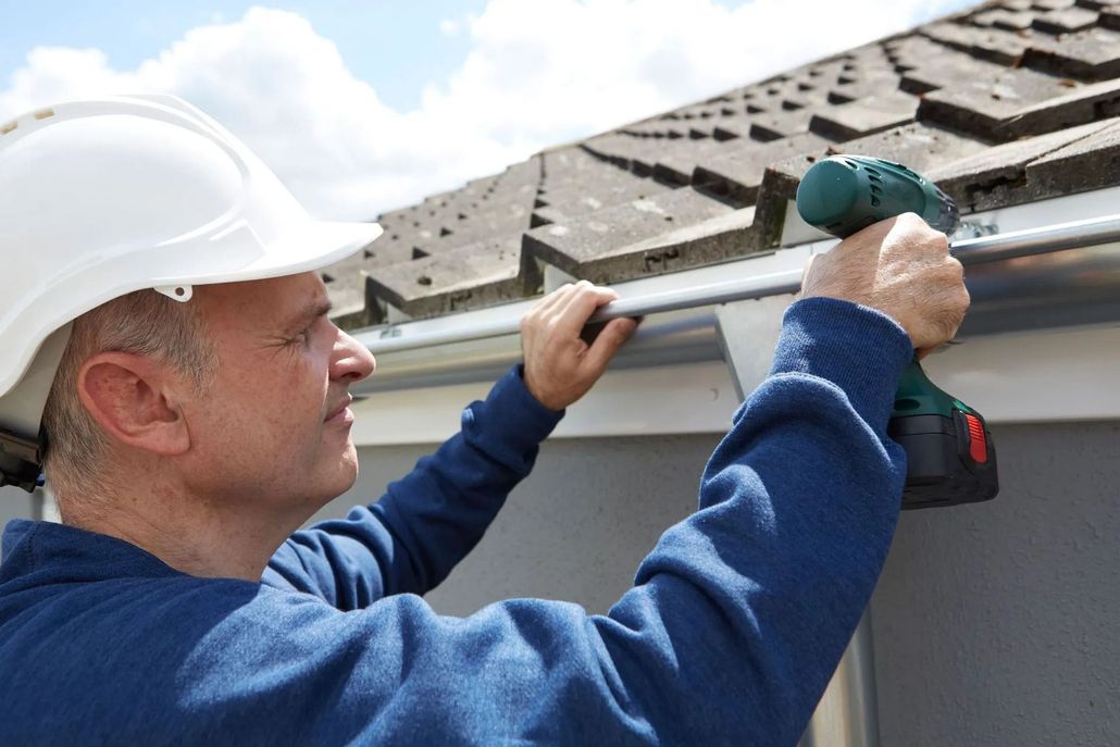 Man in hard hat installing gutter with power drill.