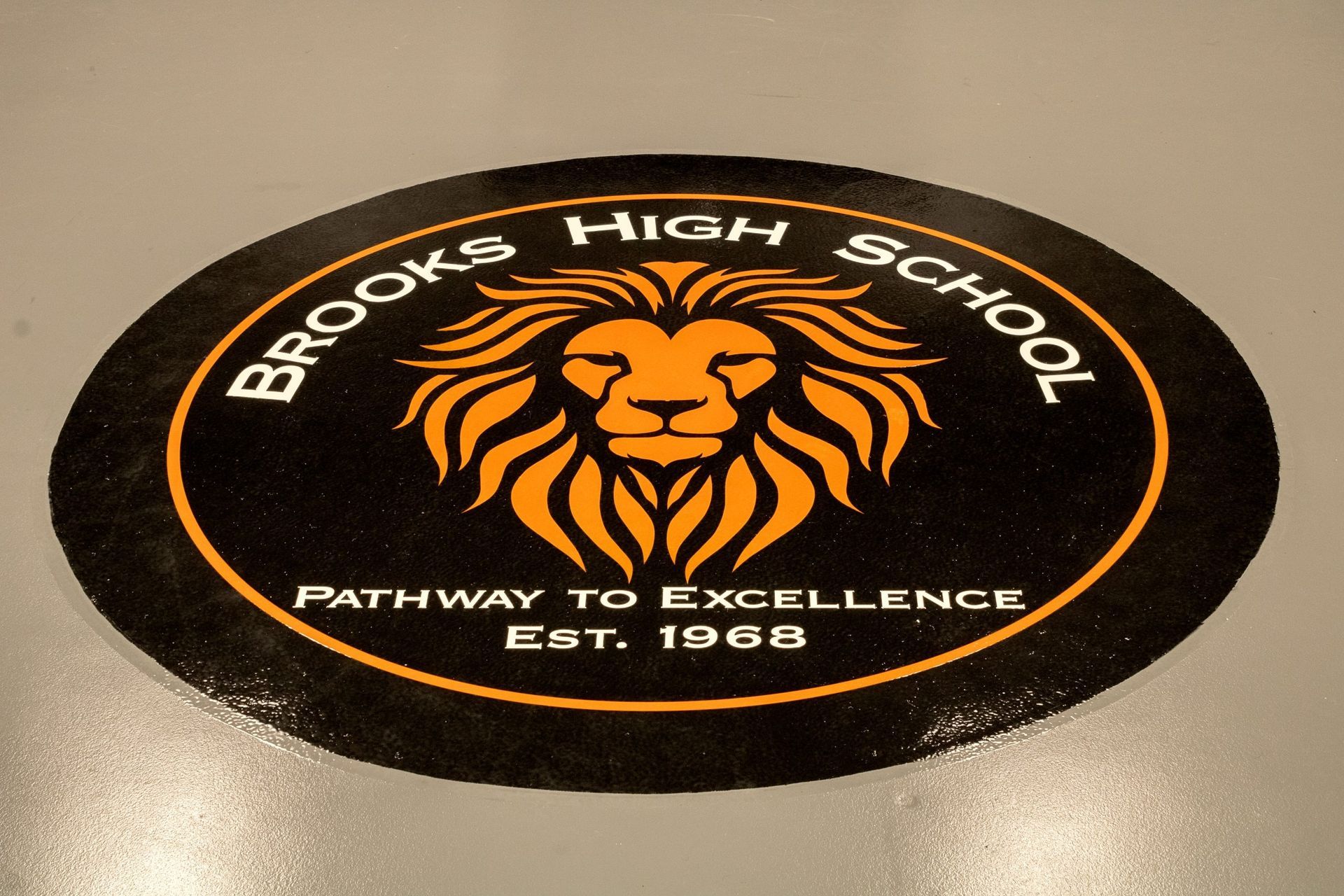 Logo for Brooks High School: Black oval with an orange lion head and text 