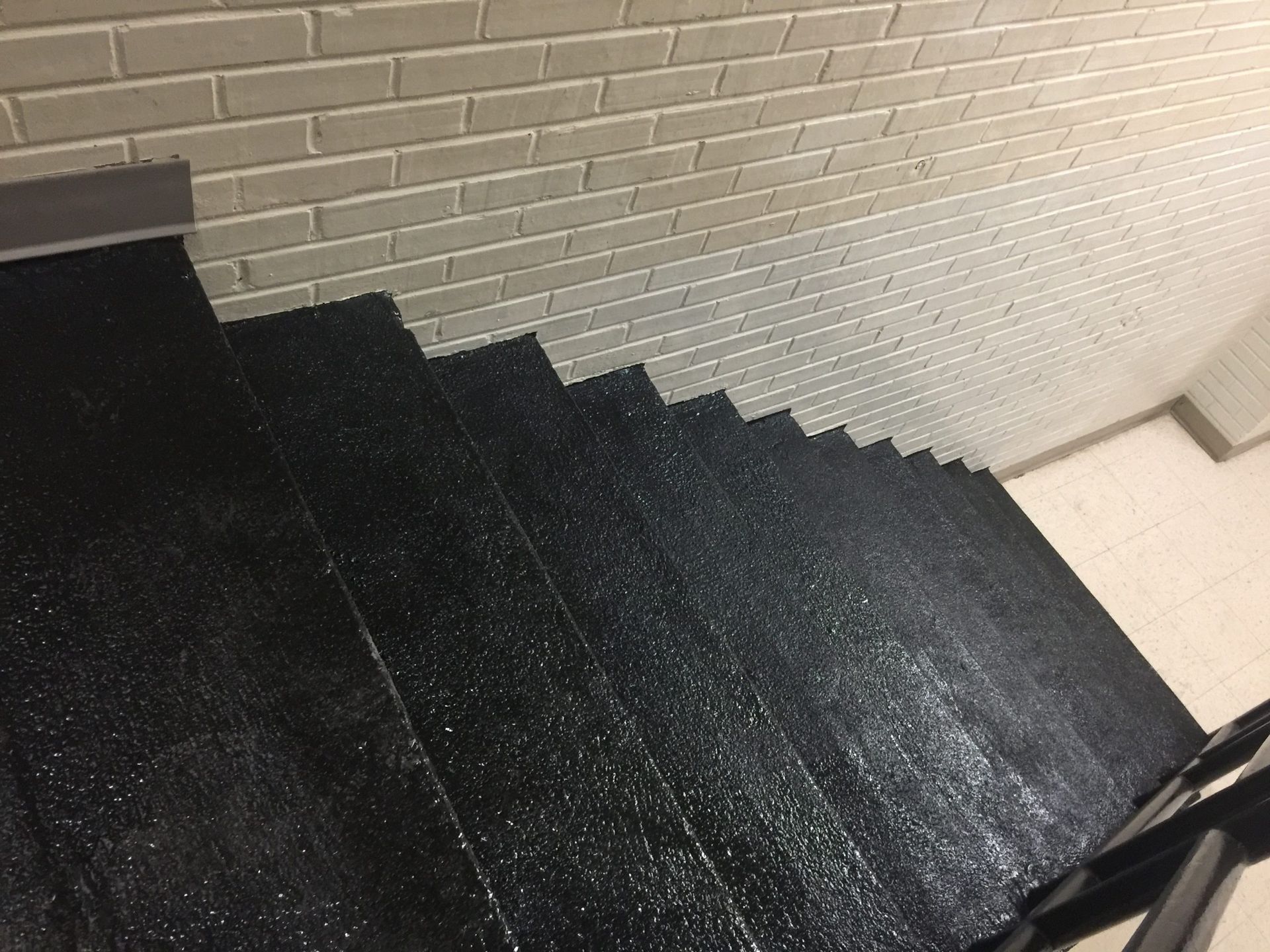 Black stairs leading down, textured surface. Light brick wall above.