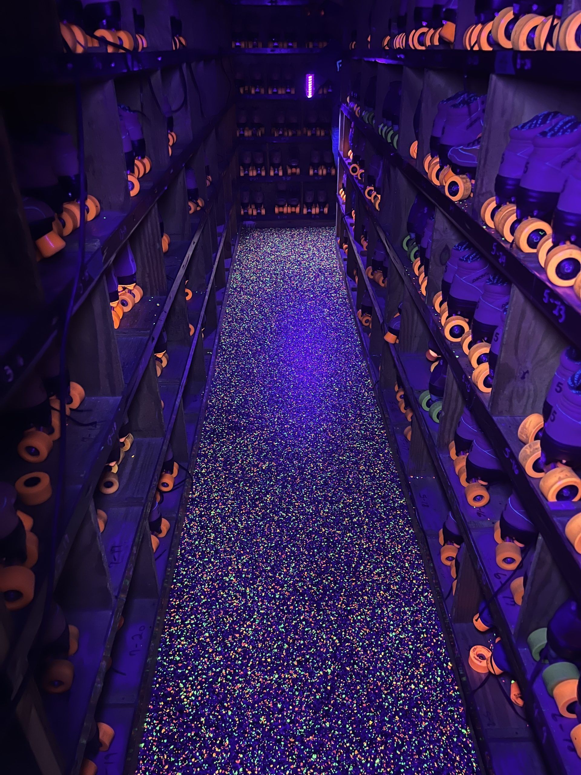 Rows of roller skates under blacklights, neon orange wheels and glowing floor.