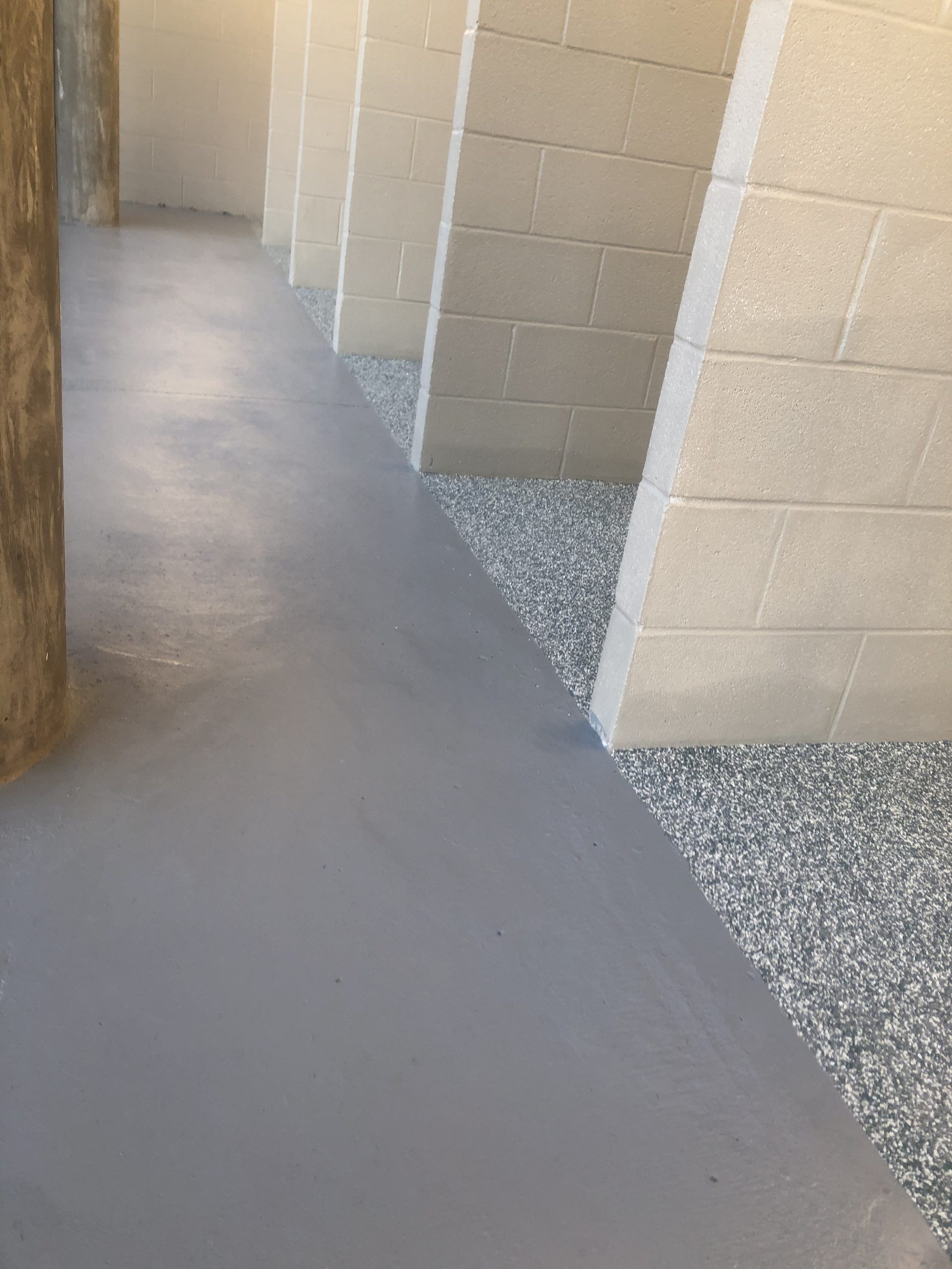 Gray concrete floor with gravel border next to concrete block wall.