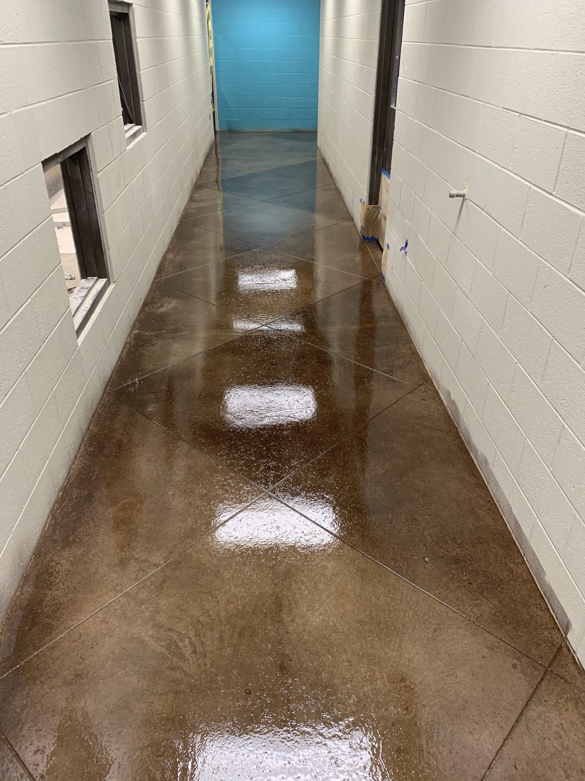Long, narrow hallway with polished brown concrete floor and white brick walls; teal wall at end.