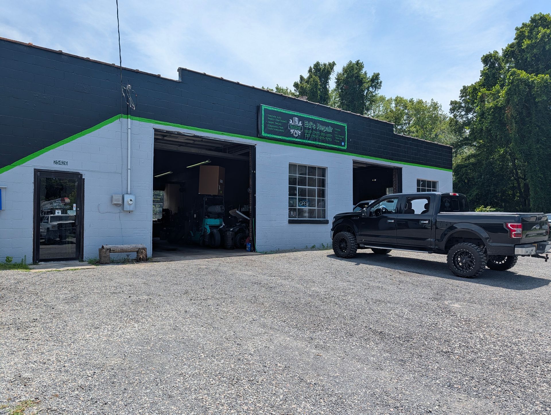 Auto repair shop with open garage bays, a black pickup truck parked outside, and gravel lot.
