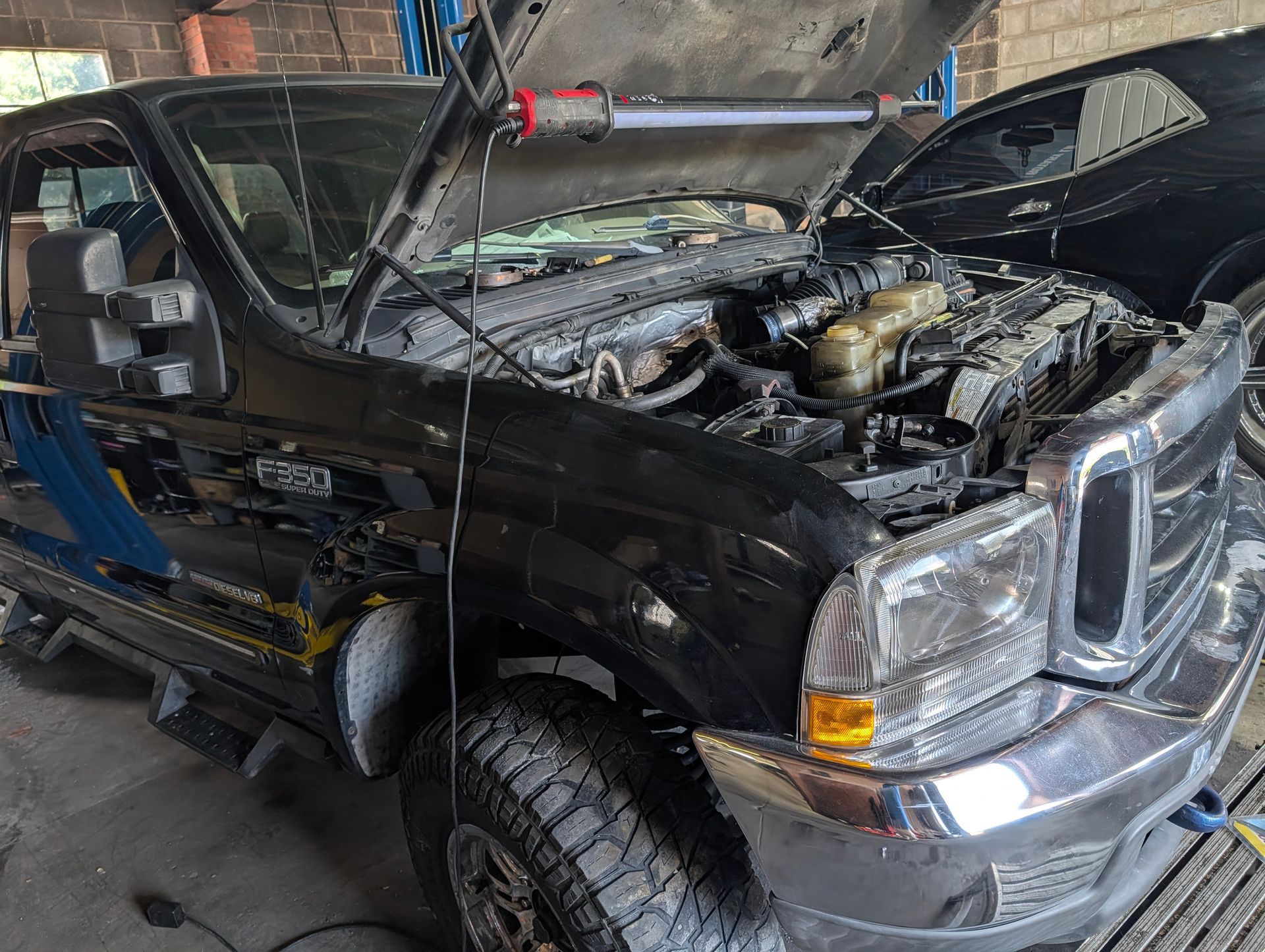 Black pickup truck in a garage, hood open and engine exposed, with visible front-end damage.