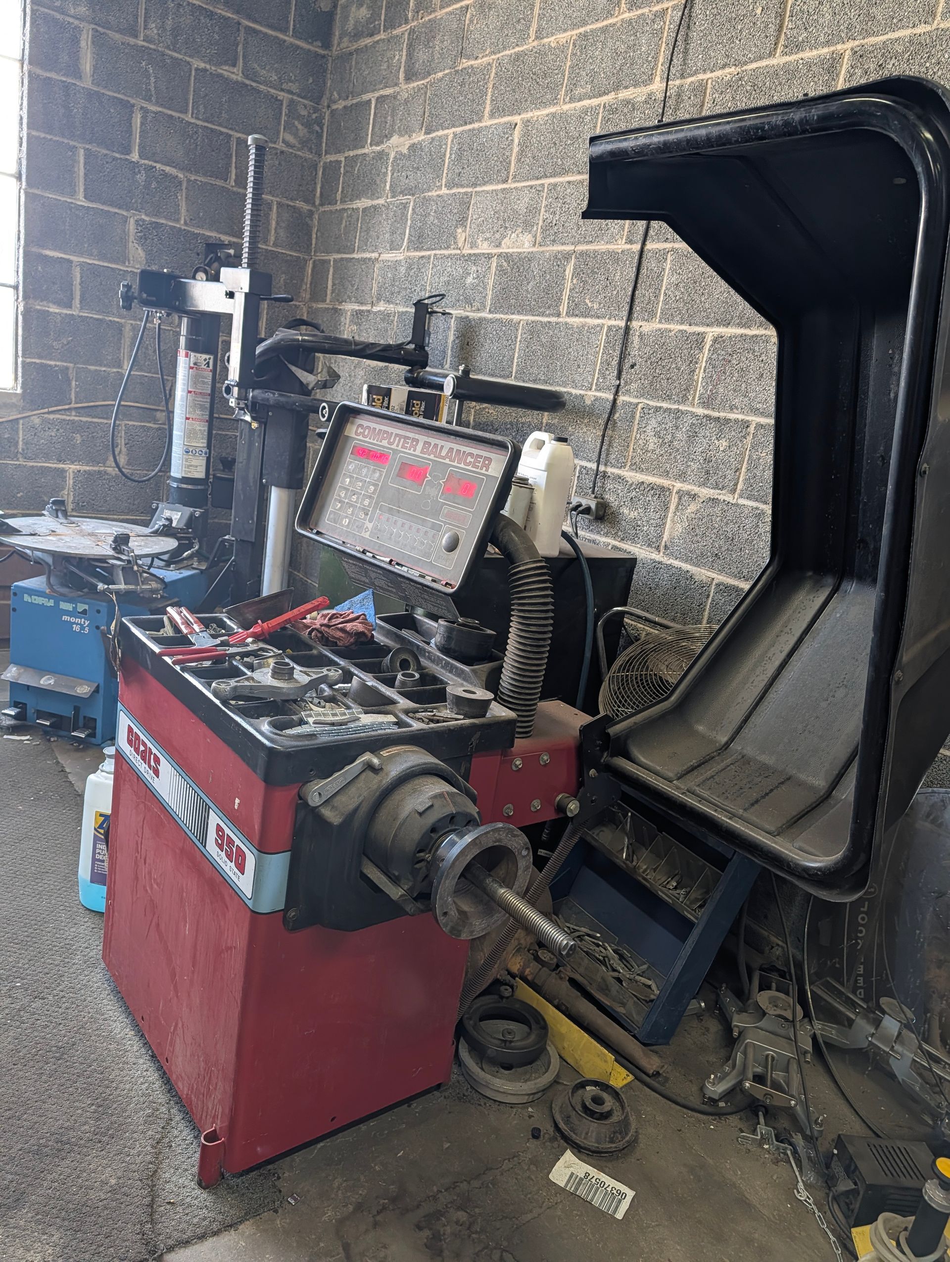 Red automotive wheel balancer in a garage, with tools and parts scattered nearby.