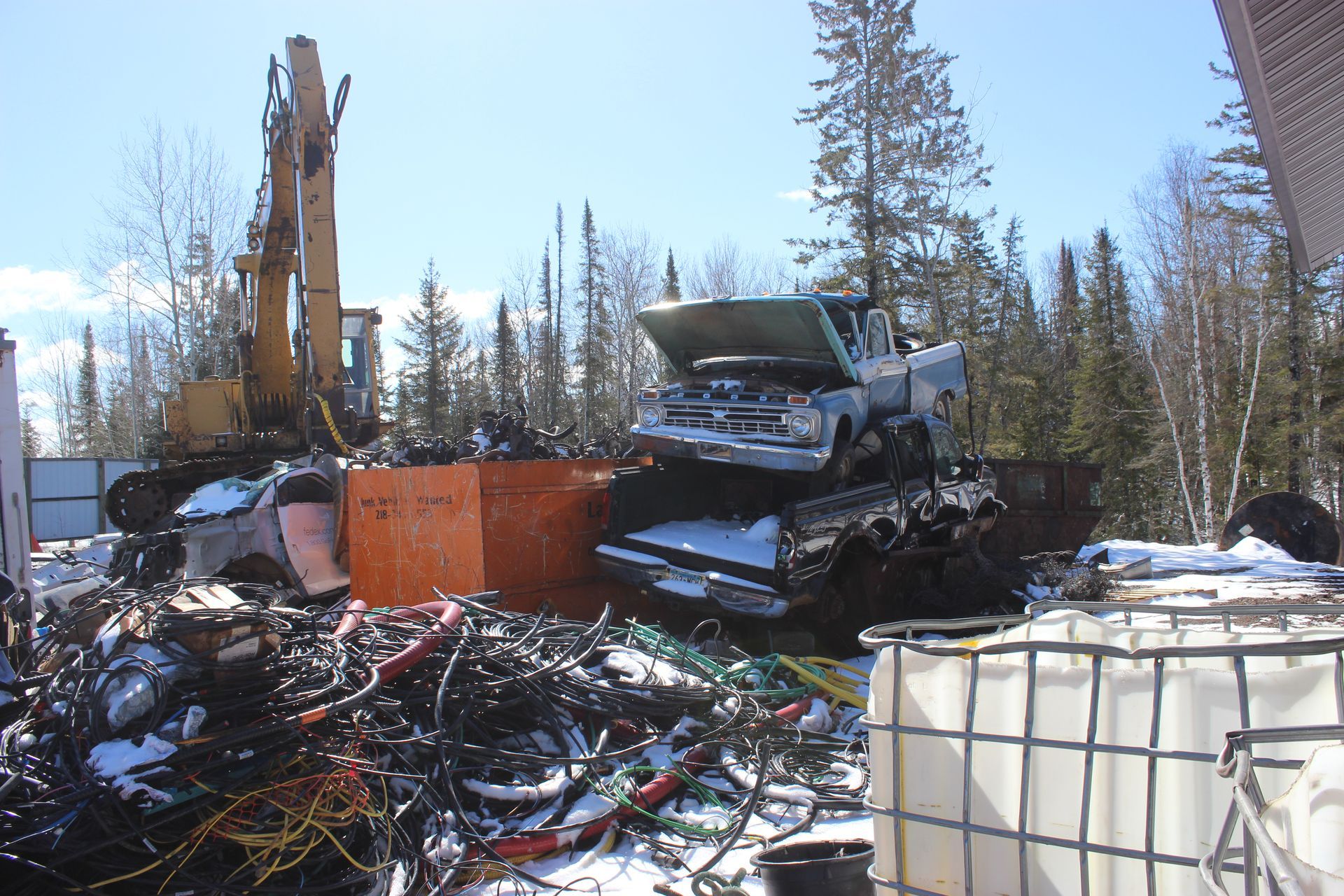Pile of scrap metal with a truck being lifted by an excavator in a snowy outdoor junkyard.
