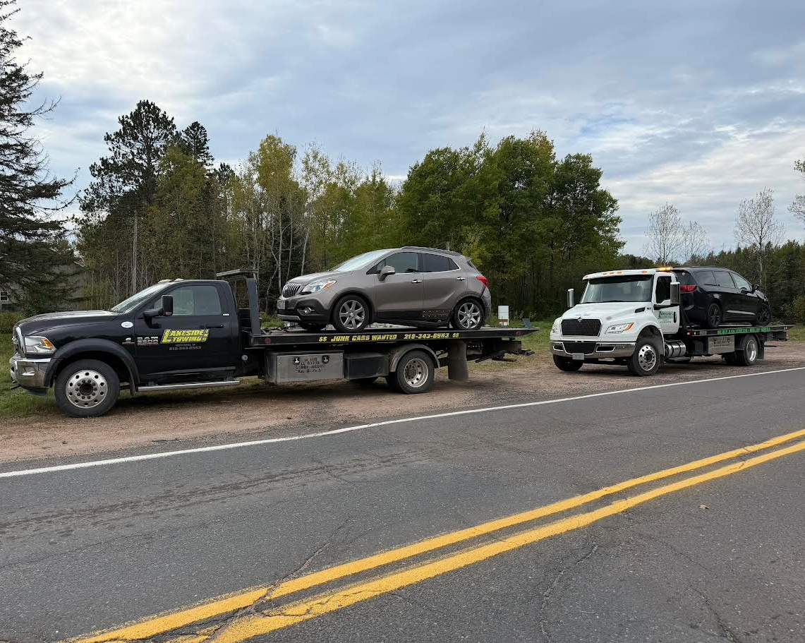 White truck stuck in muddy terrain being pulled by a yellow skid steer.