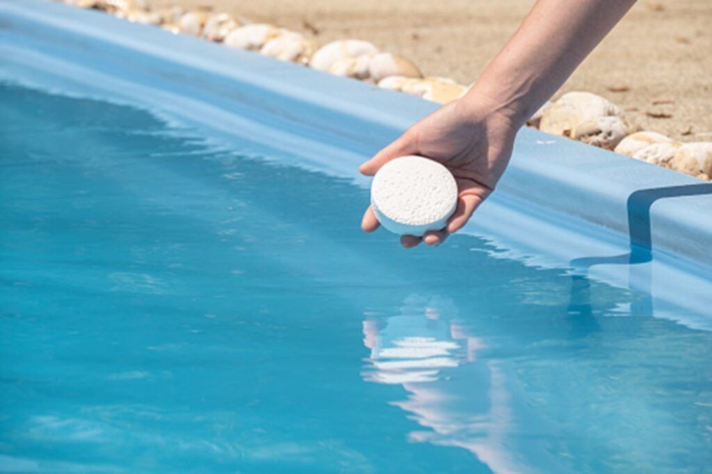 A person is holding a chemical tablet in their hand in a swimming pool.