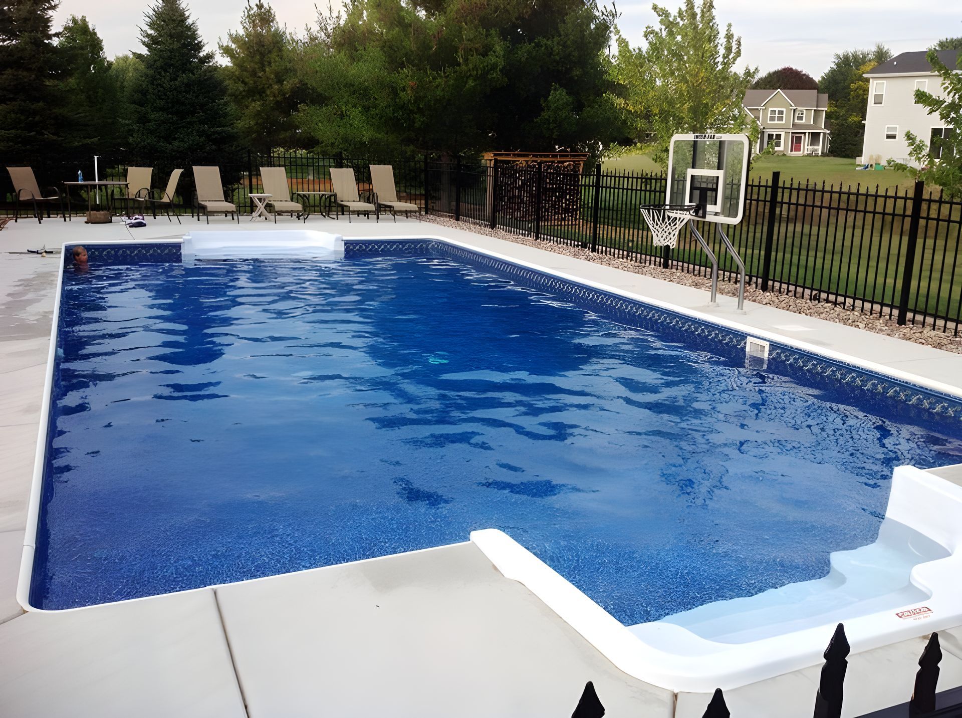 A large swimming pool surrounded by chairs and a basketball hoop