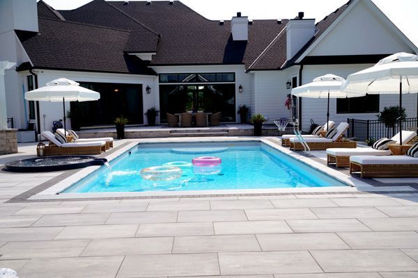 A large swimming pool surrounded by chairs and umbrellas in front of a house