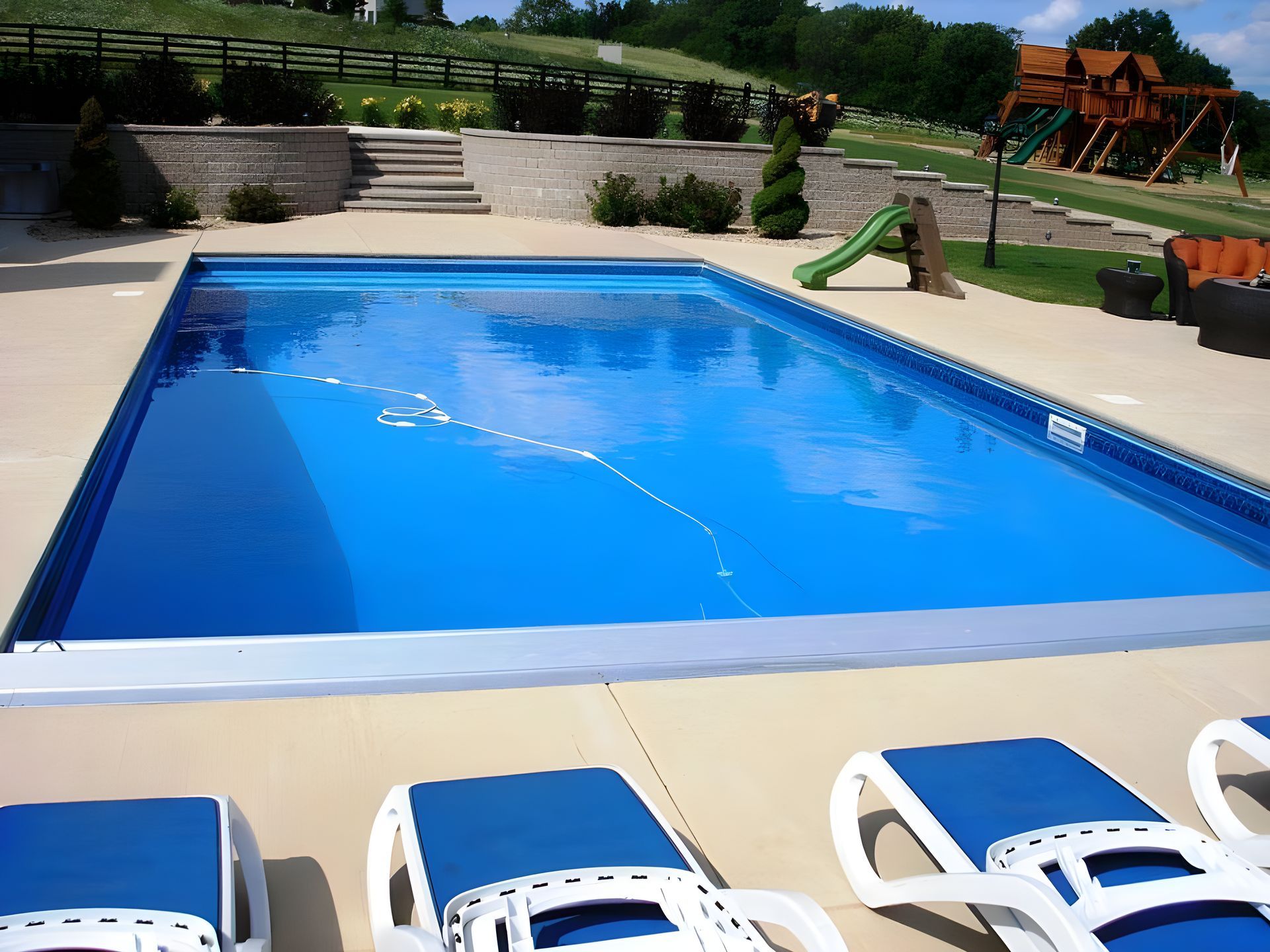 A large swimming pool with blue chairs in front of it