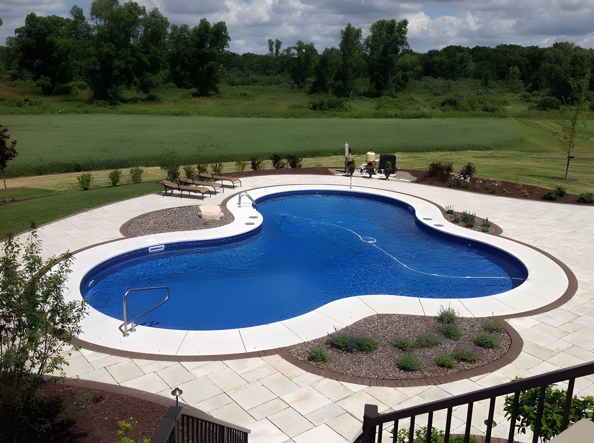 A large swimming pool is surrounded by a patio and trees
