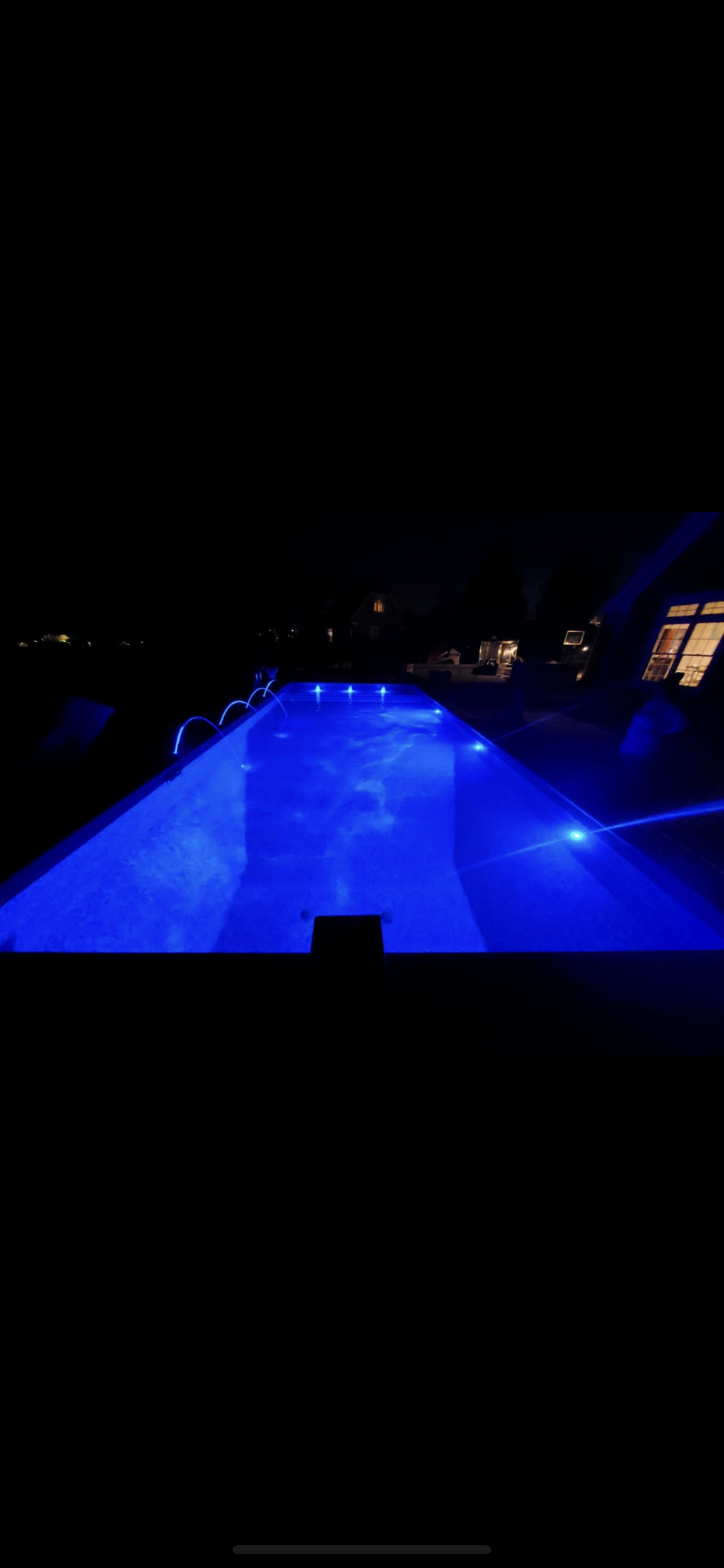 A swimming pool is lit up at night with blue lights.