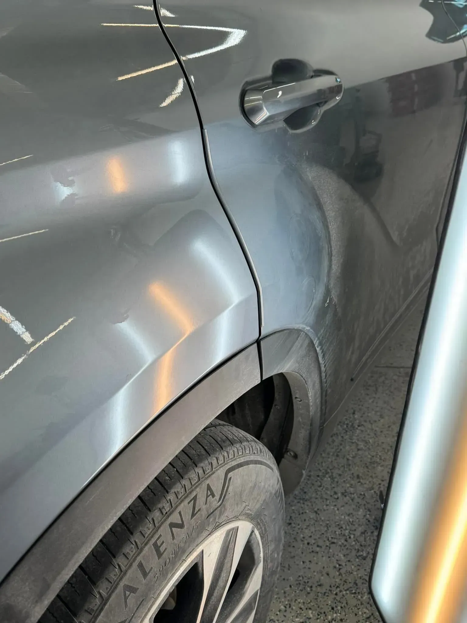 Gray car door with dent and tire visible.