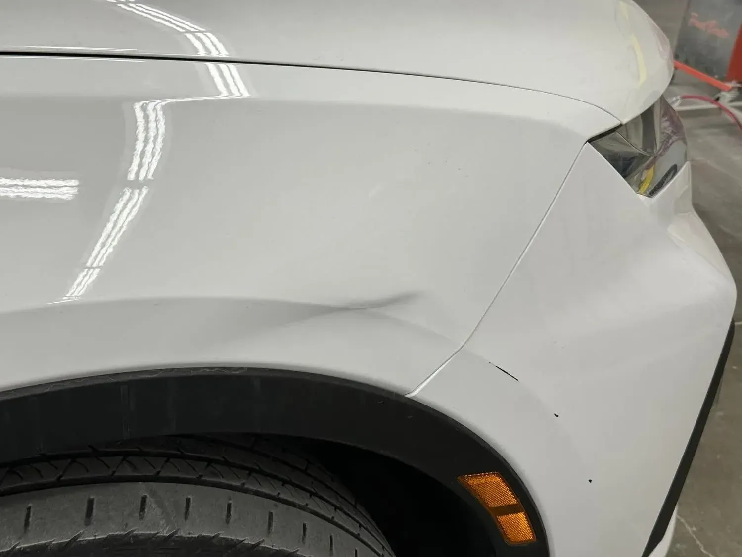 White car front fender with a dent, tire visible.