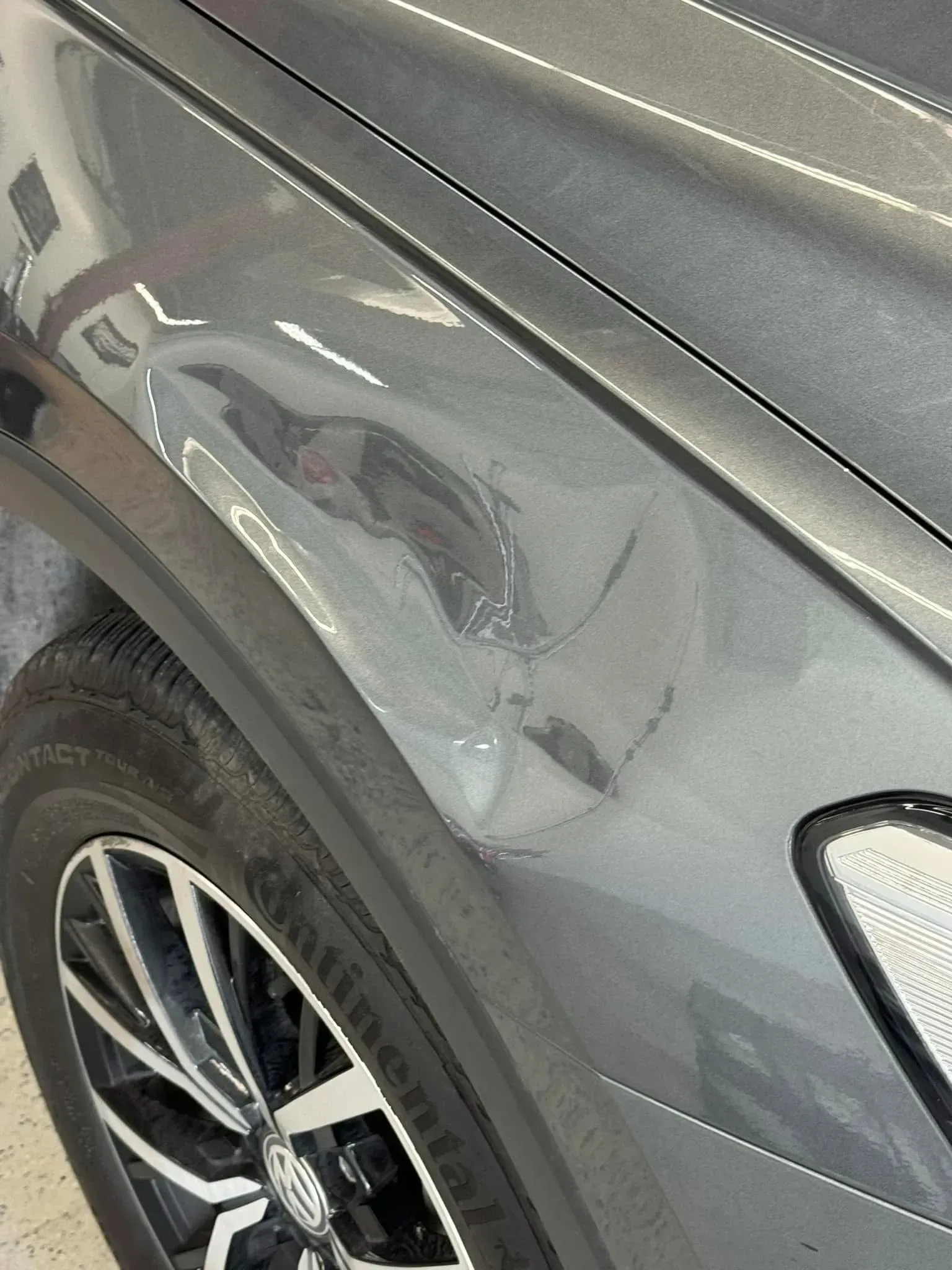Damaged gray car fender with dent and scratches near a tire.