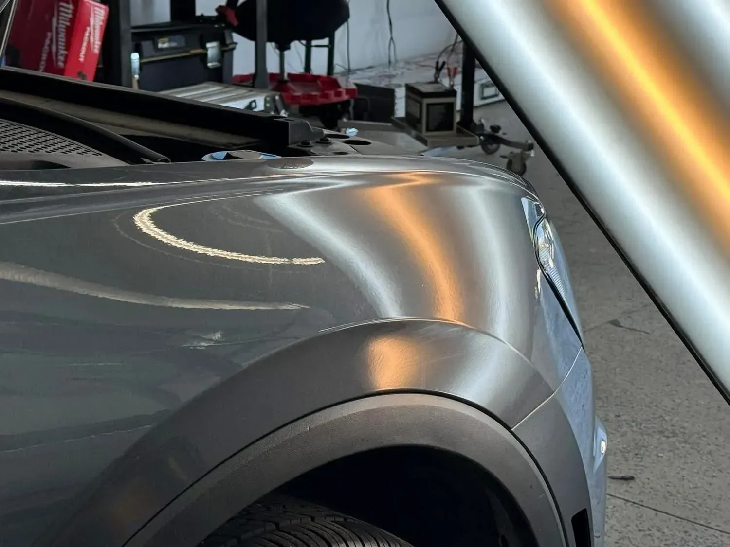 A grey car fender with reflection lights, undergoing dent repair in a shop.