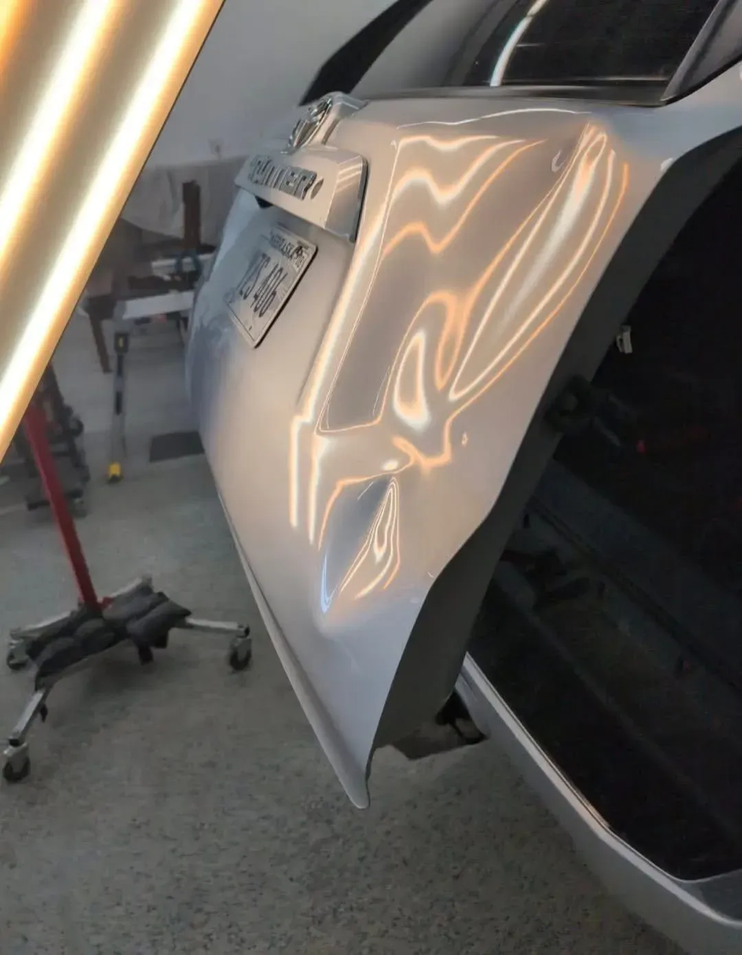 Silver car rear quarter panel with a dent, lit by a dent repair light.