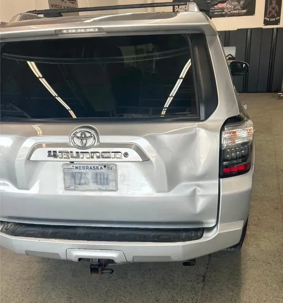 Silver Toyota 4Runner with rear damage, dented bumper, in a garage.