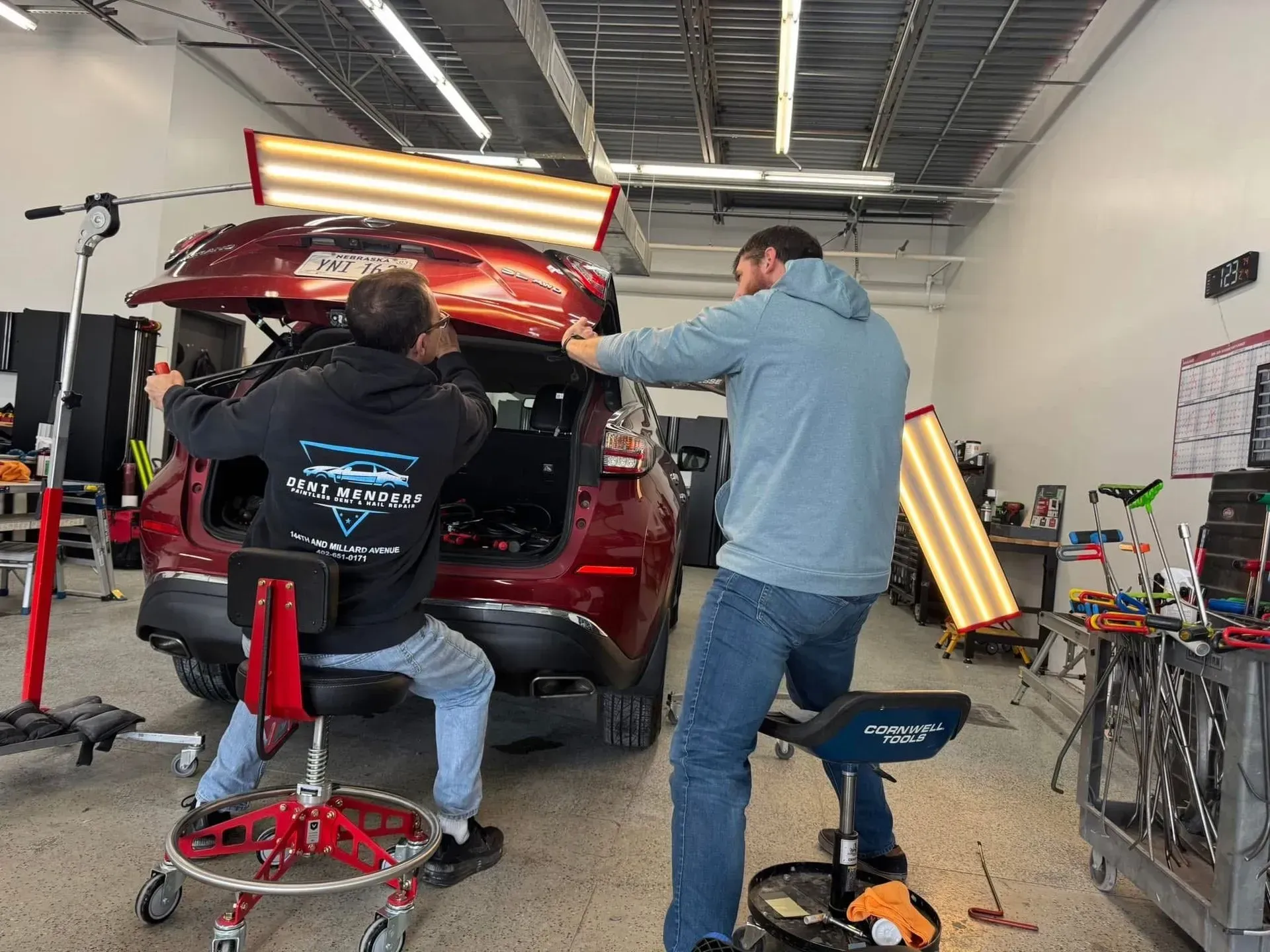 Two men working on a red car in a repair shop, using light to assess damage.