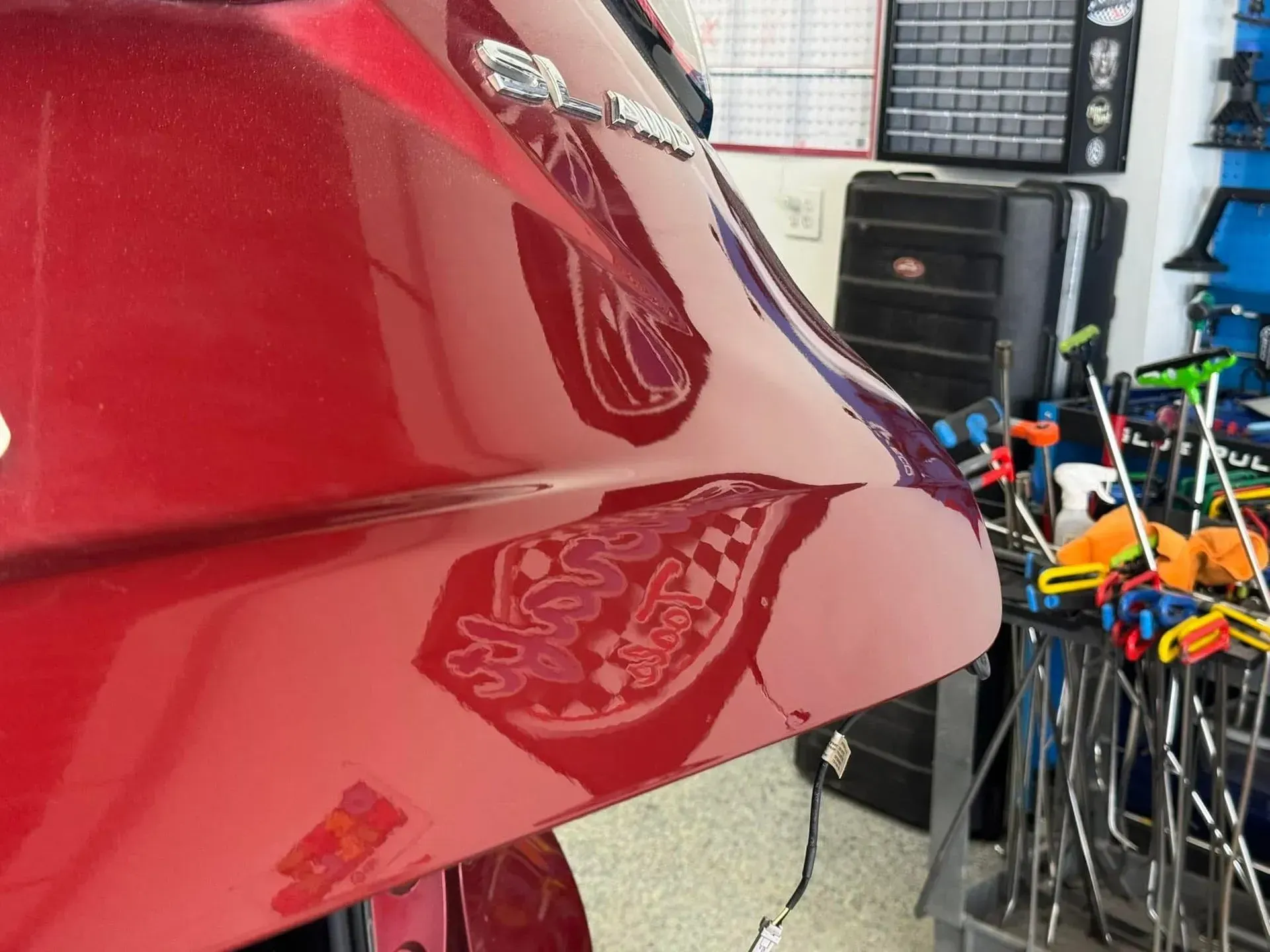 Red car panel with reflections of objects in a workshop, including clamps and tools.