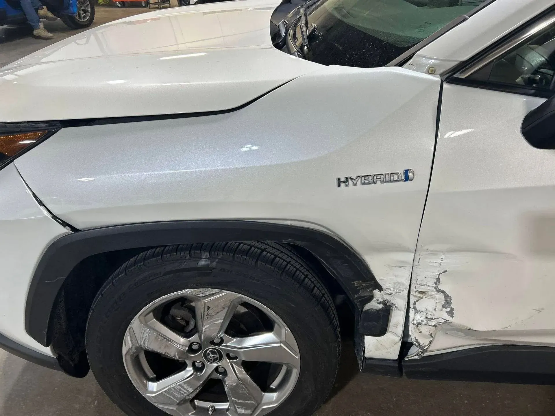White Toyota RAV4 Hybrid with front-end damage; dented fender, crumpled panel near wheel.