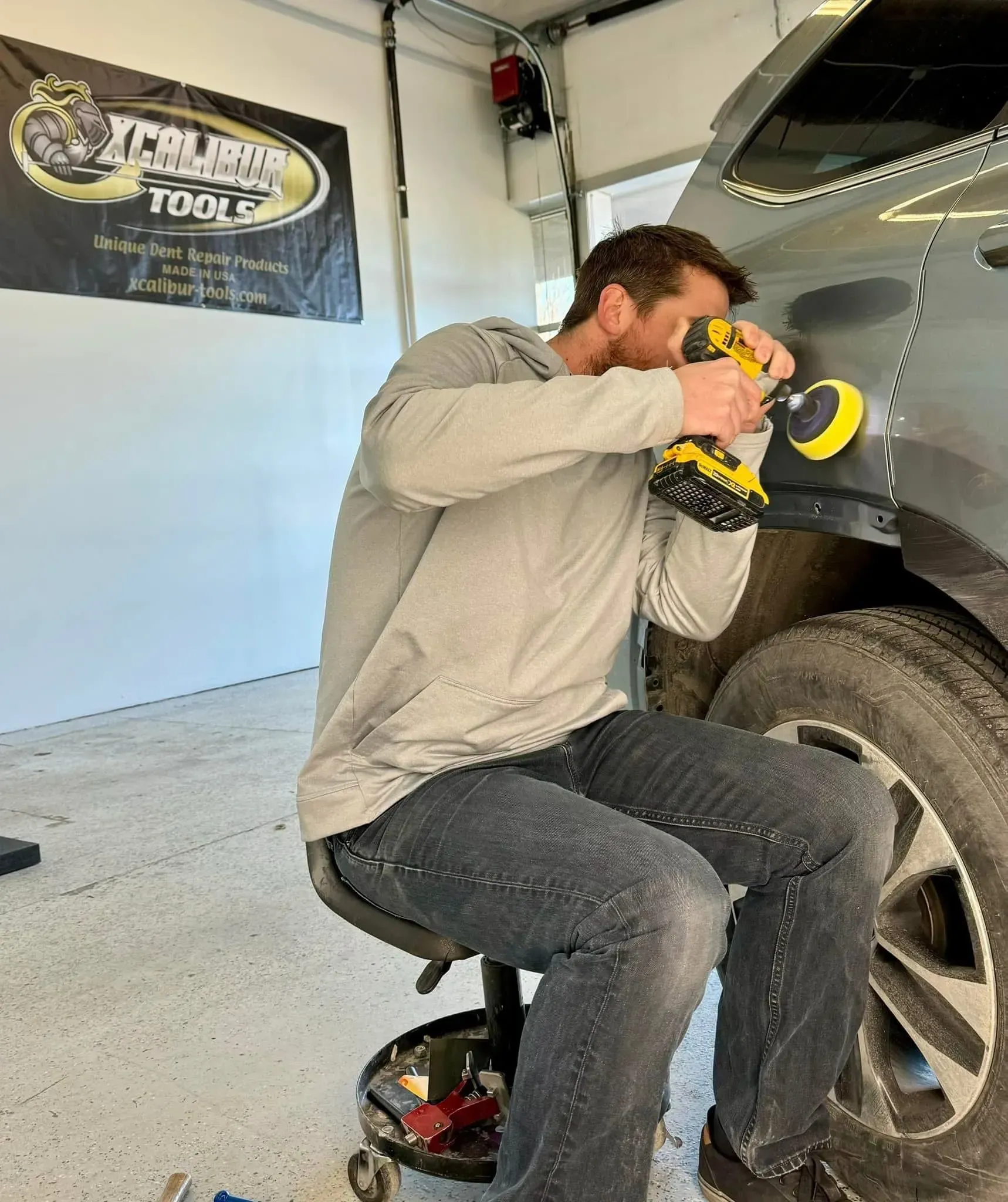 Man using a power tool to work on a car's body in a garage.
