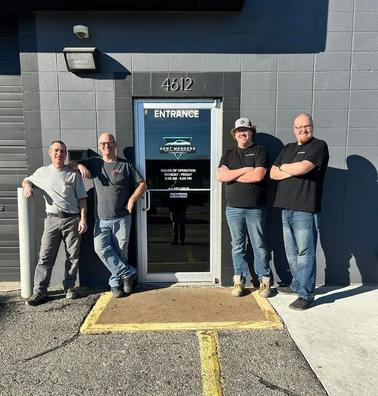 Four men stand in front of a building entrance with 