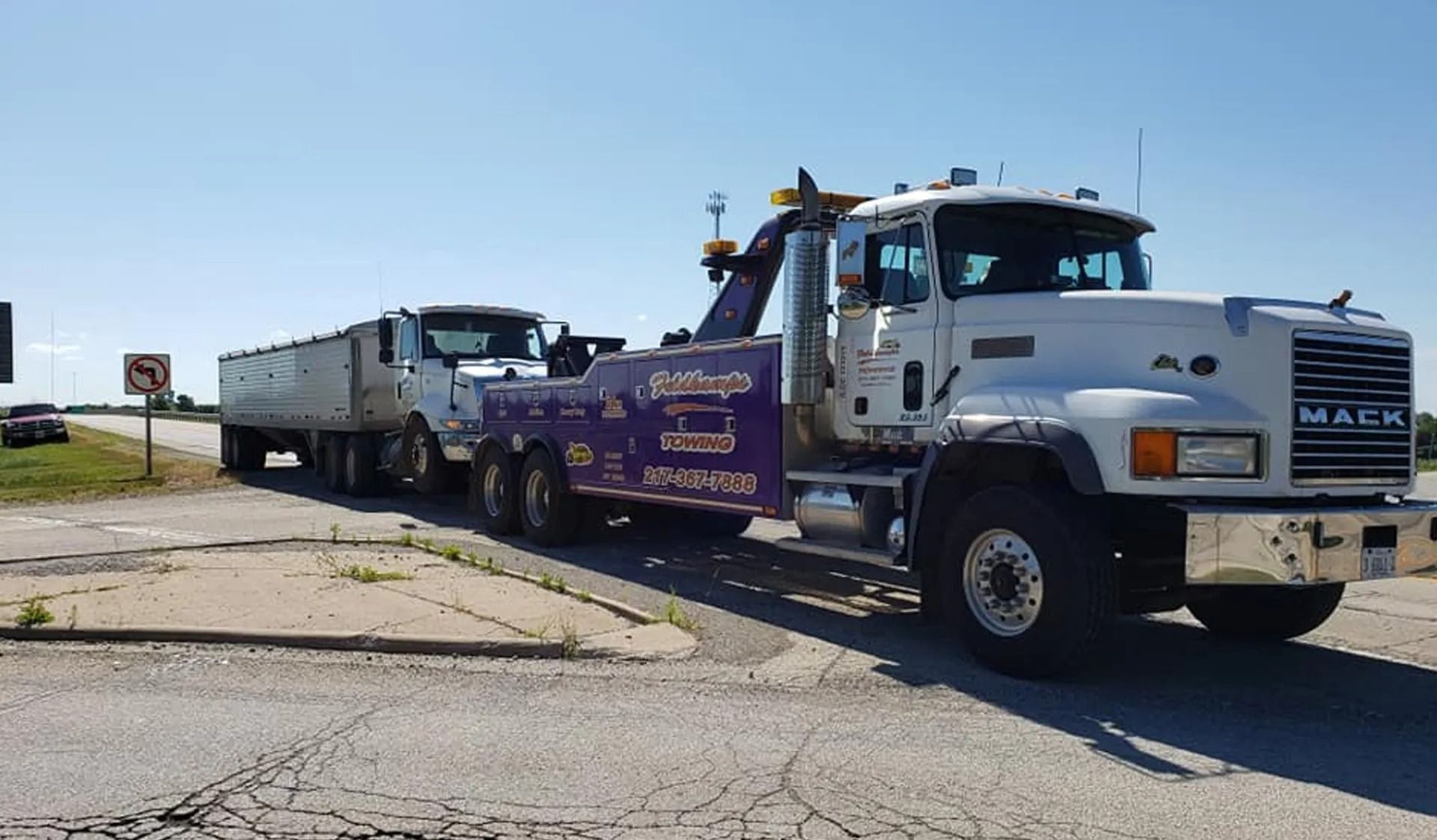 Tow truck towing a semi-truck with a trailer on a cracked road, sunny day.
