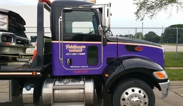 Tow truck, purple and black with company logo, towing a vehicle.