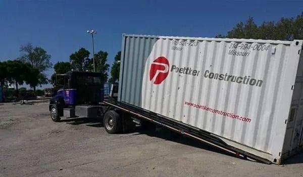 A flatbed truck carrying a large white shipping container with 