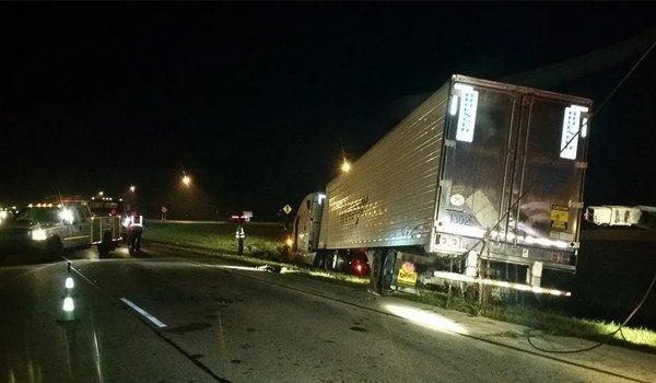 Semi-truck tilted on side of road at night with emergency personnel present.