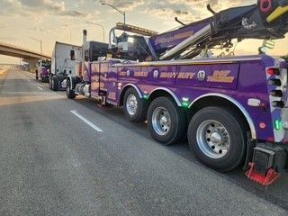Purple heavy-duty tow truck on the road, with its boom extended, possibly recovering a vehicle.