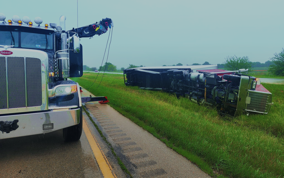 Tow truck at the roadside, lifting an overturned semi-trailer in wet conditions.