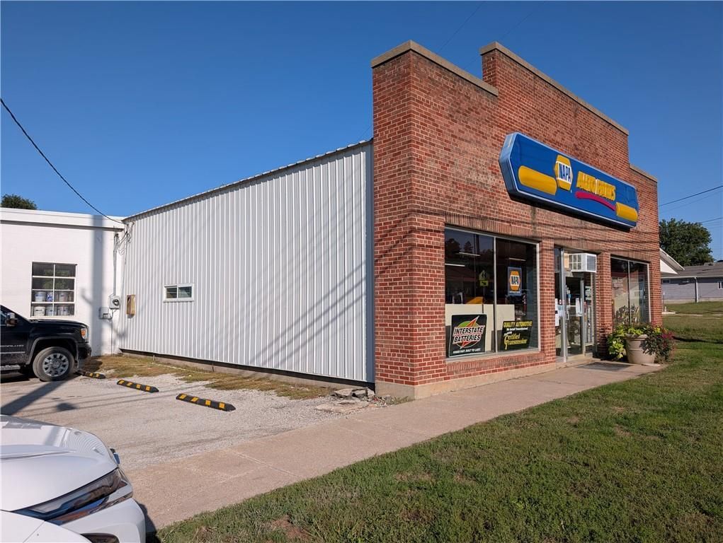 Brick storefront with blue-and-yellow sign, glass windows, and white metal siding on a sunny street corner