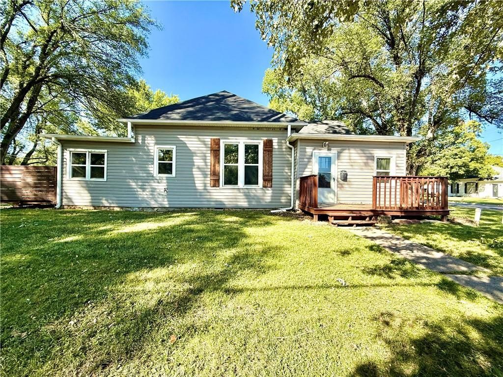 Single-story white house with a front deck and a large green lawn under trees