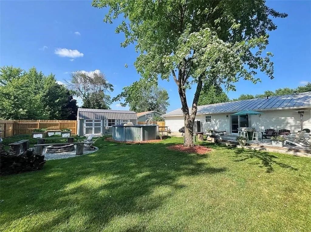 Sunny backyard with green lawn, large tree, and small outbuildings under a blue sky