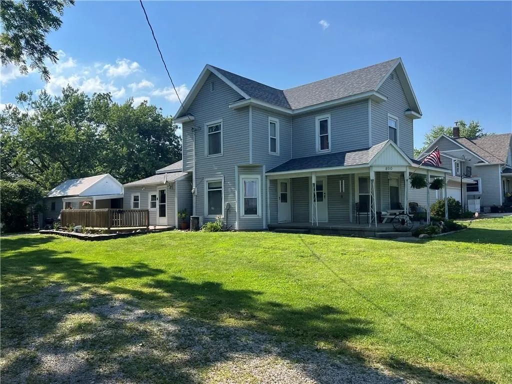 Two-story gray house with a porch and large green lawn under a sunny blue sky
