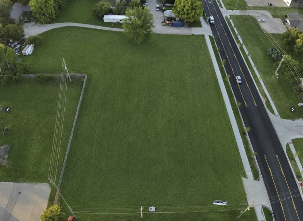 Aerial view of a large green field beside a road and nearby houses.