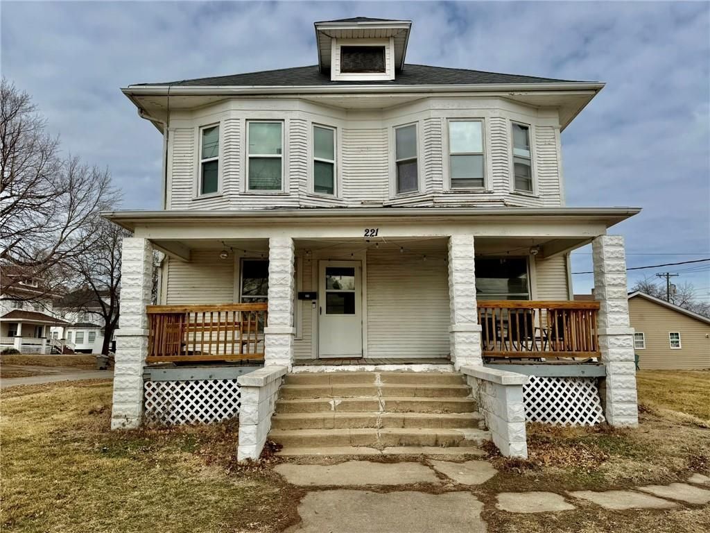 Front view of a two-story white house with a porch, steps, and dormer windows on an overcast day